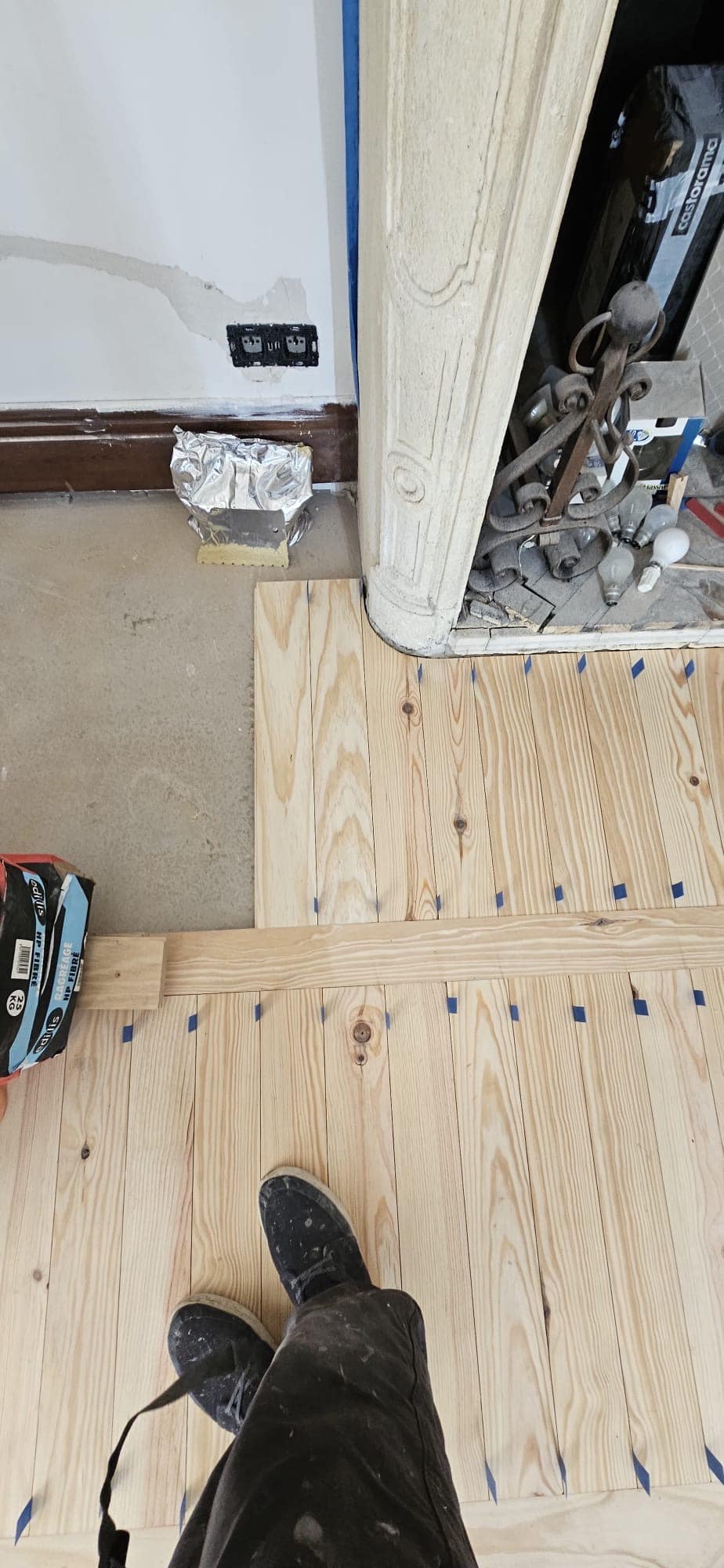 Installation d'un plancher en pin massif autour d'une cheminée ancienne avec repères au ruban bleu.