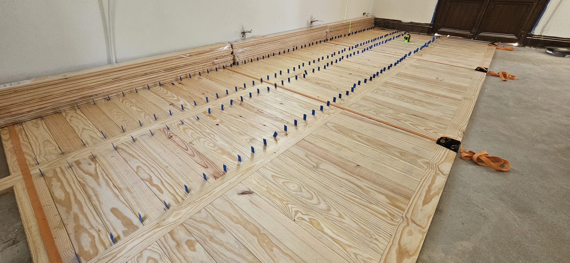 Pose d'un plancher en bois clair avec sangles de serrage et cales d'espacement pour une rénovation de sol.