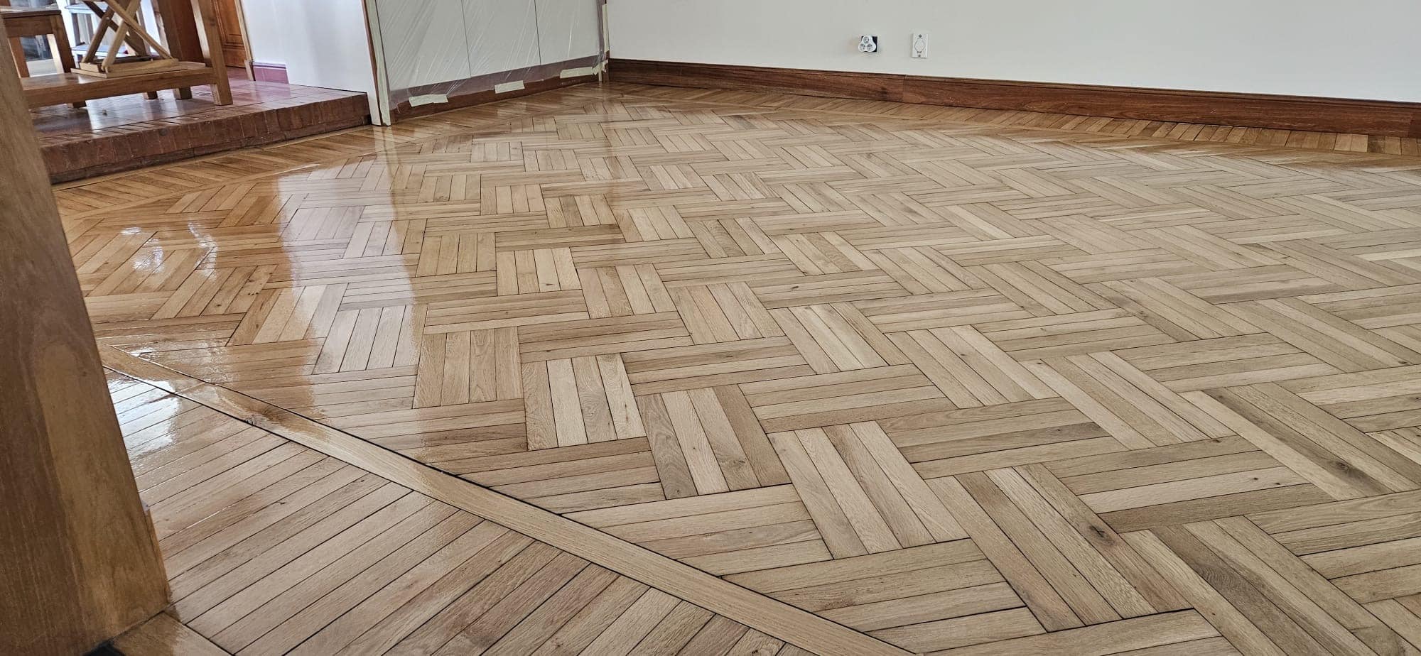 Parquet en chêne à motif damier en cours de vitrification, montrant le contraste entre bois brut et vernis brillant.
