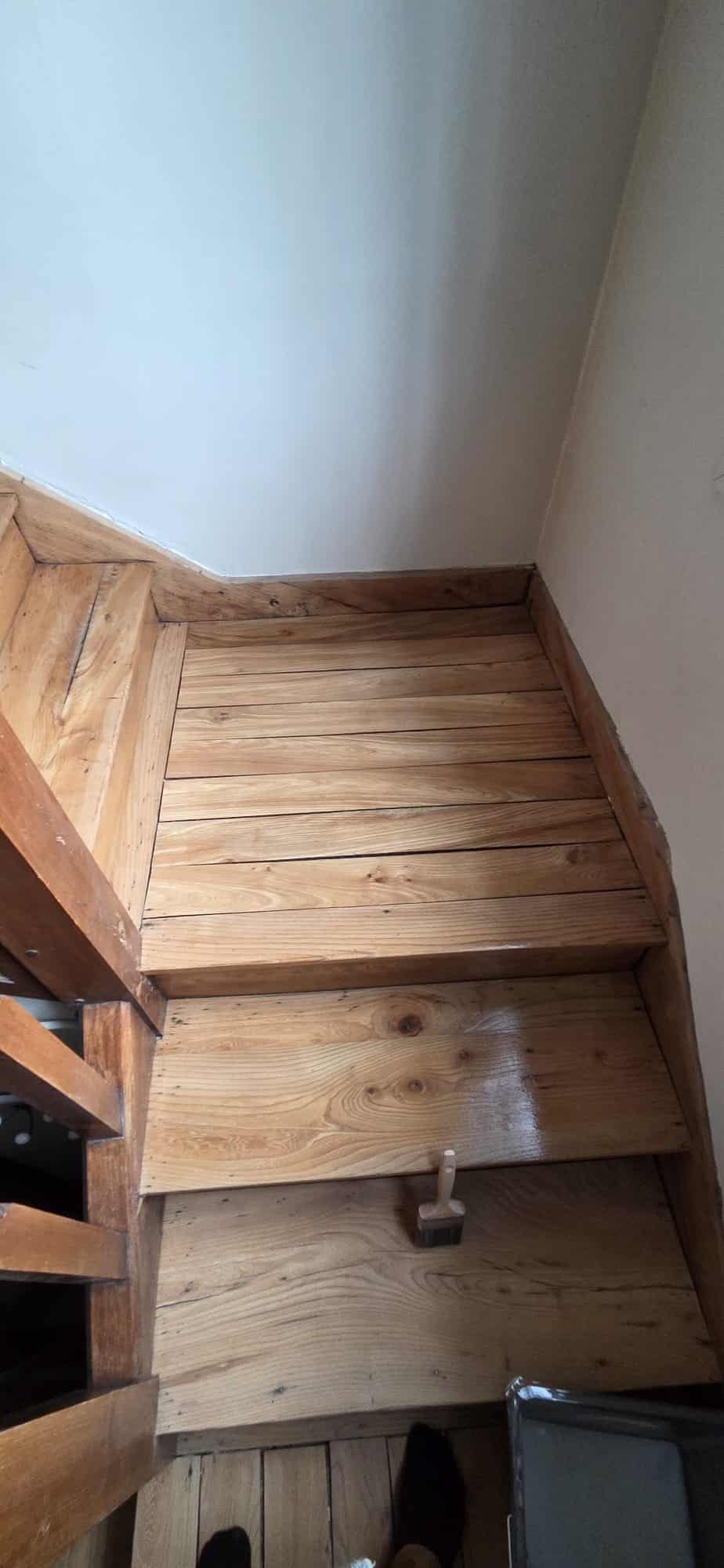 Vitrification d'un escalier en bois avec un pinceau sur une marche fraîchement vernie pour une rénovation intérieure.