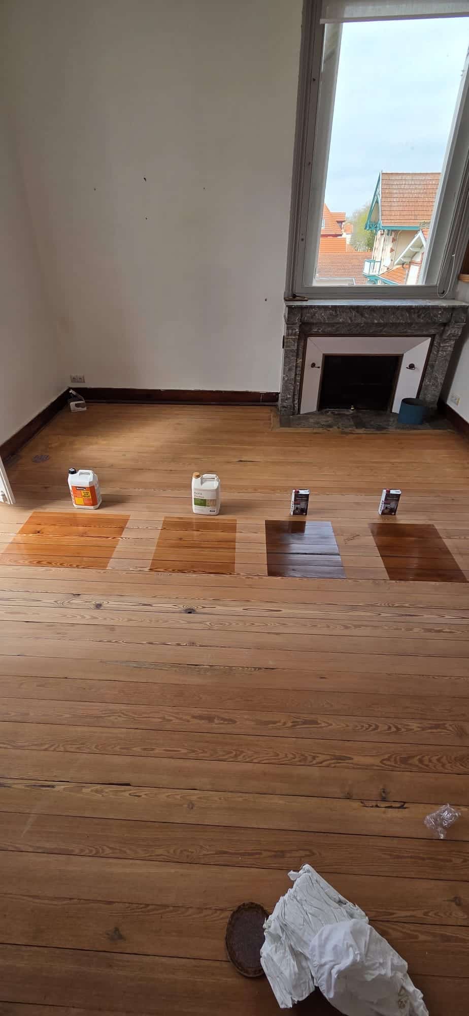 Échantillons de teintes sur parquet bois, du chêne clair au noyer foncé, avec bidons de finition Bona et Rubio.