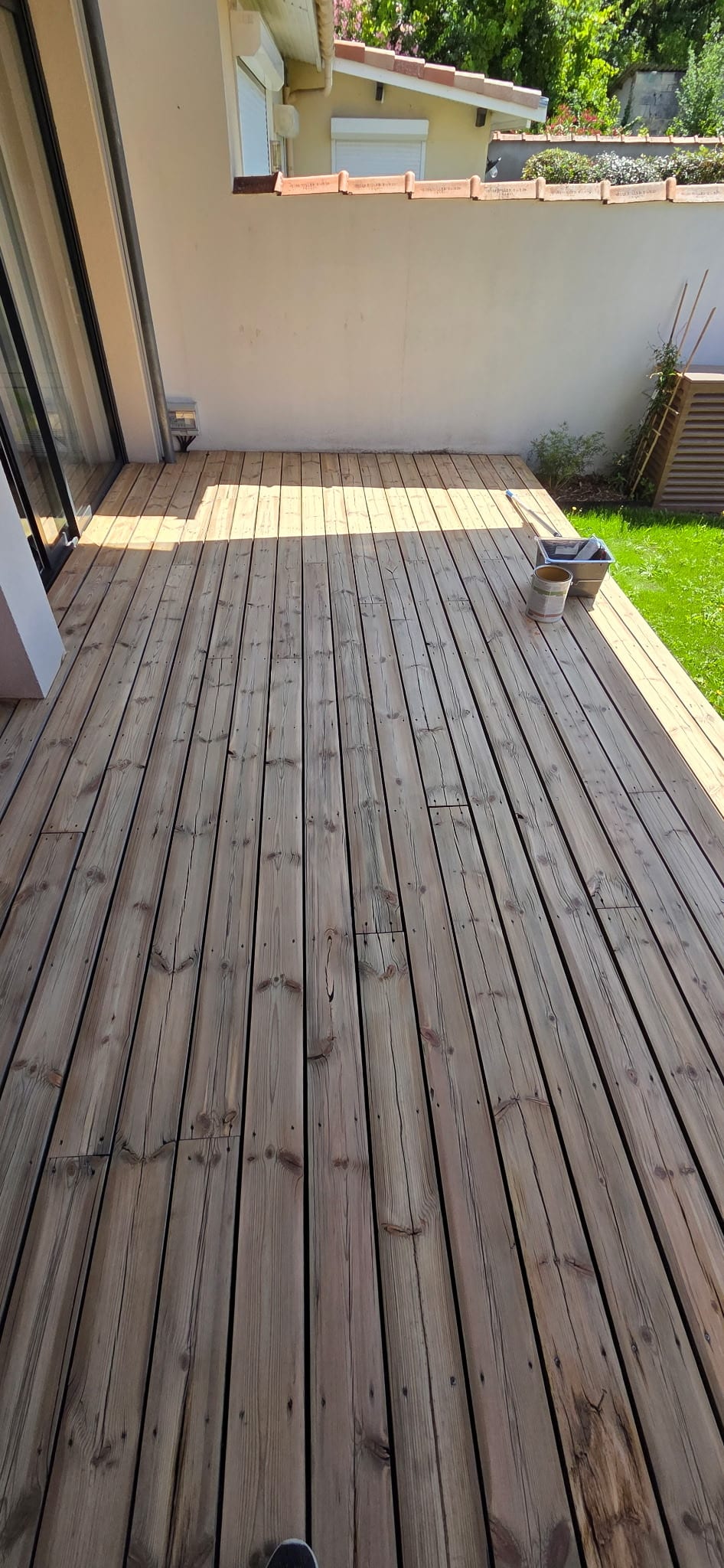 Terrasse bois en cours d'entretien avec seau et rouleau au soleil.