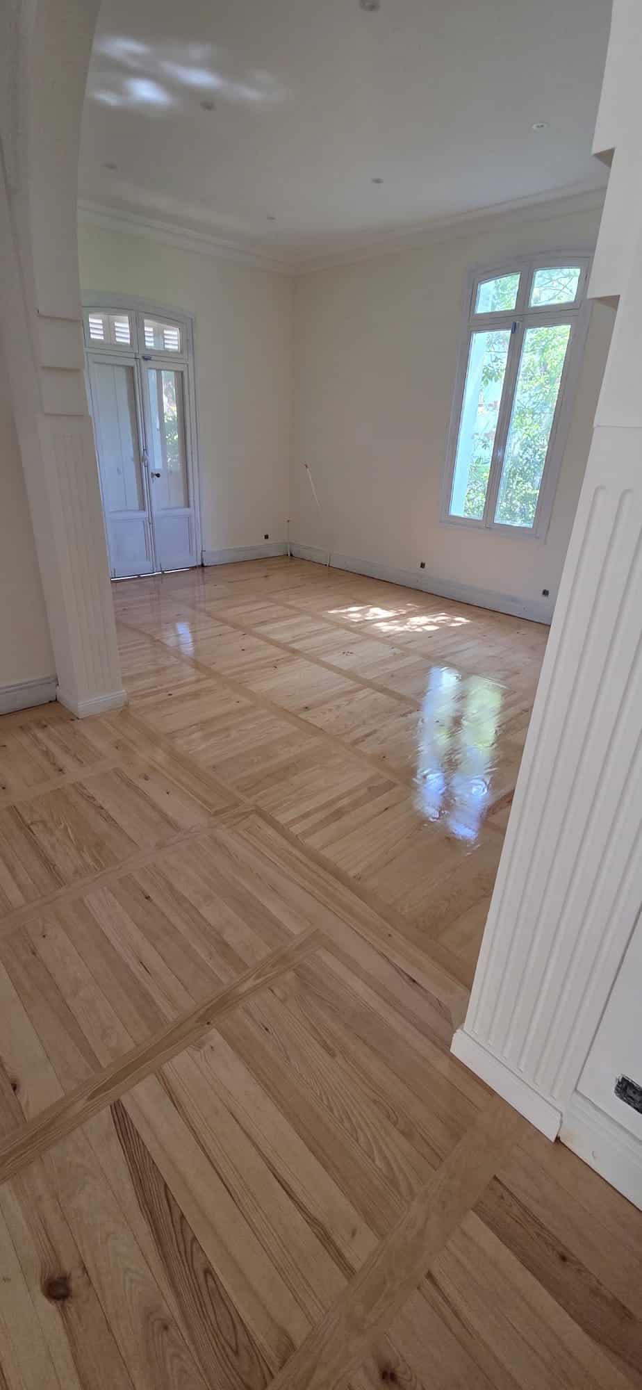 Parquet en bois massif verni au motif damier dans un intérieur lumineux avec colonnes décoratives.