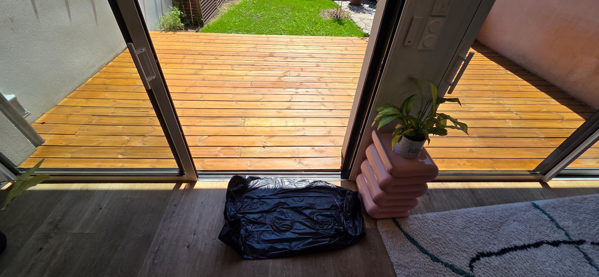 Vue intérieure sur terrasse bois ensoleillée, sac noir et plante.