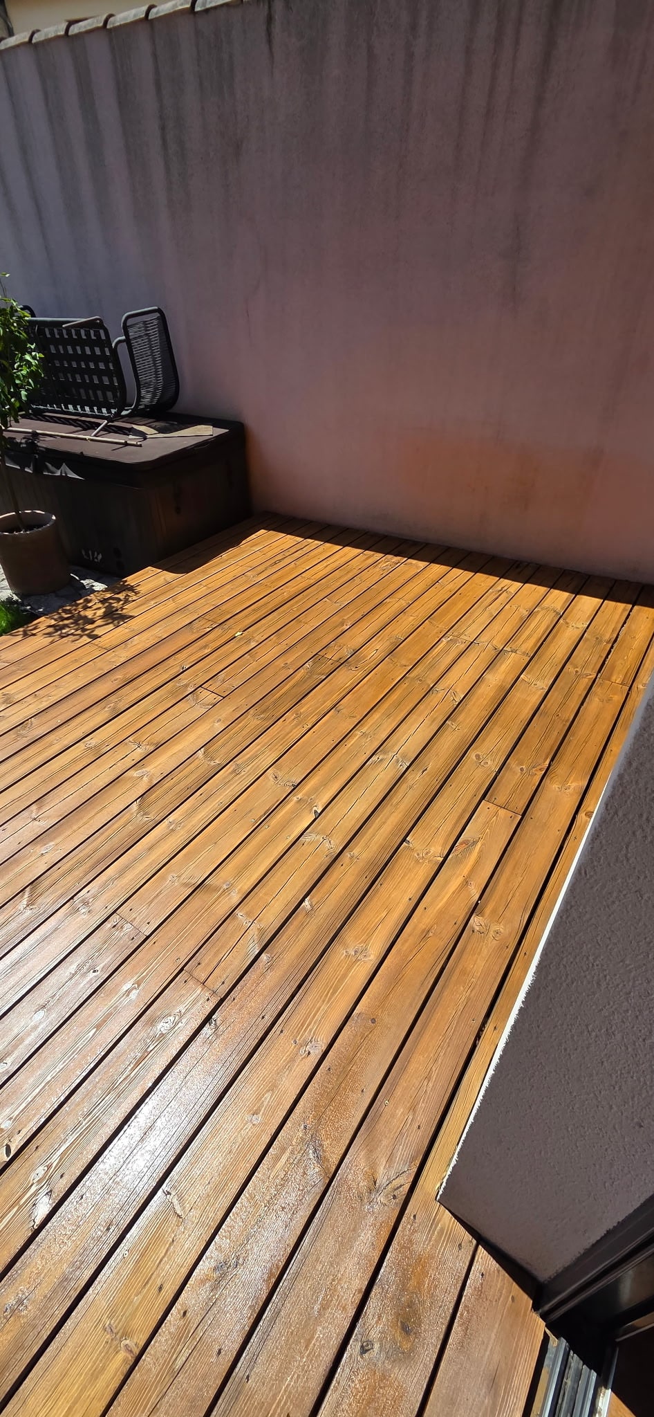 Terrasse en bois lasuré marron ensoleillée avec coffre de rangement et mur extérieur clair.