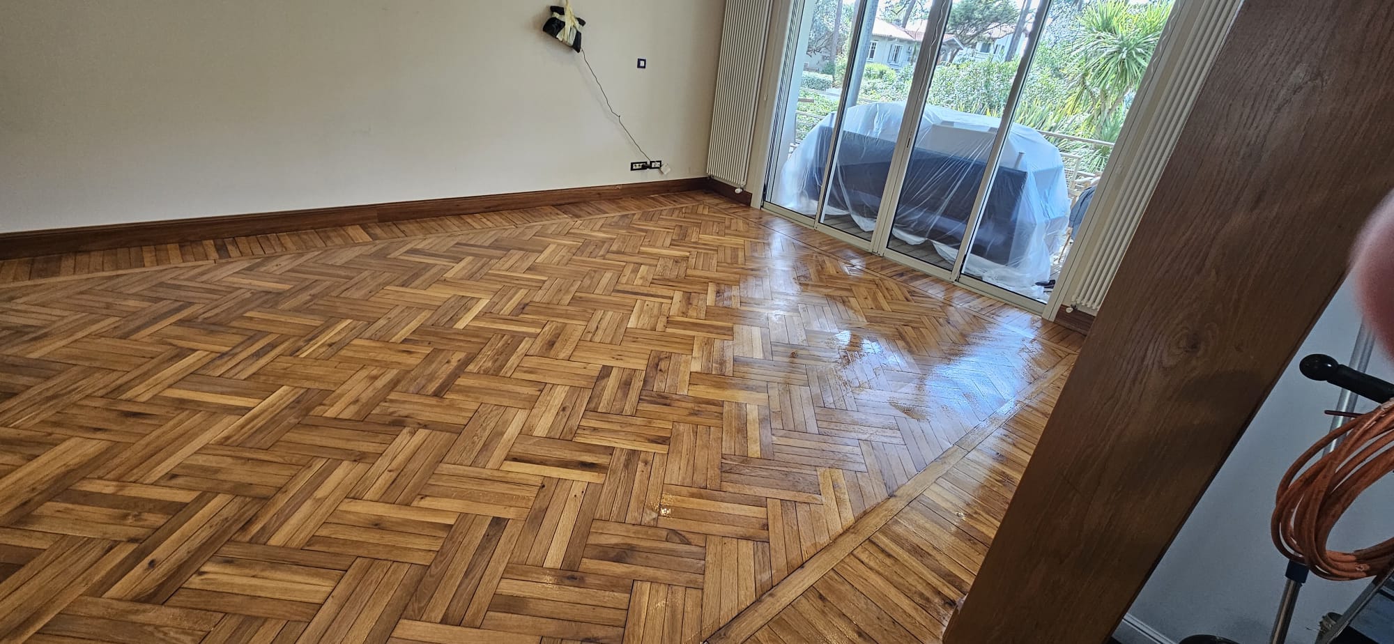 Parquet en bois vitrifié brillant avec pose en chevrons dans un salon lumineux ouvrant sur une terrasse.