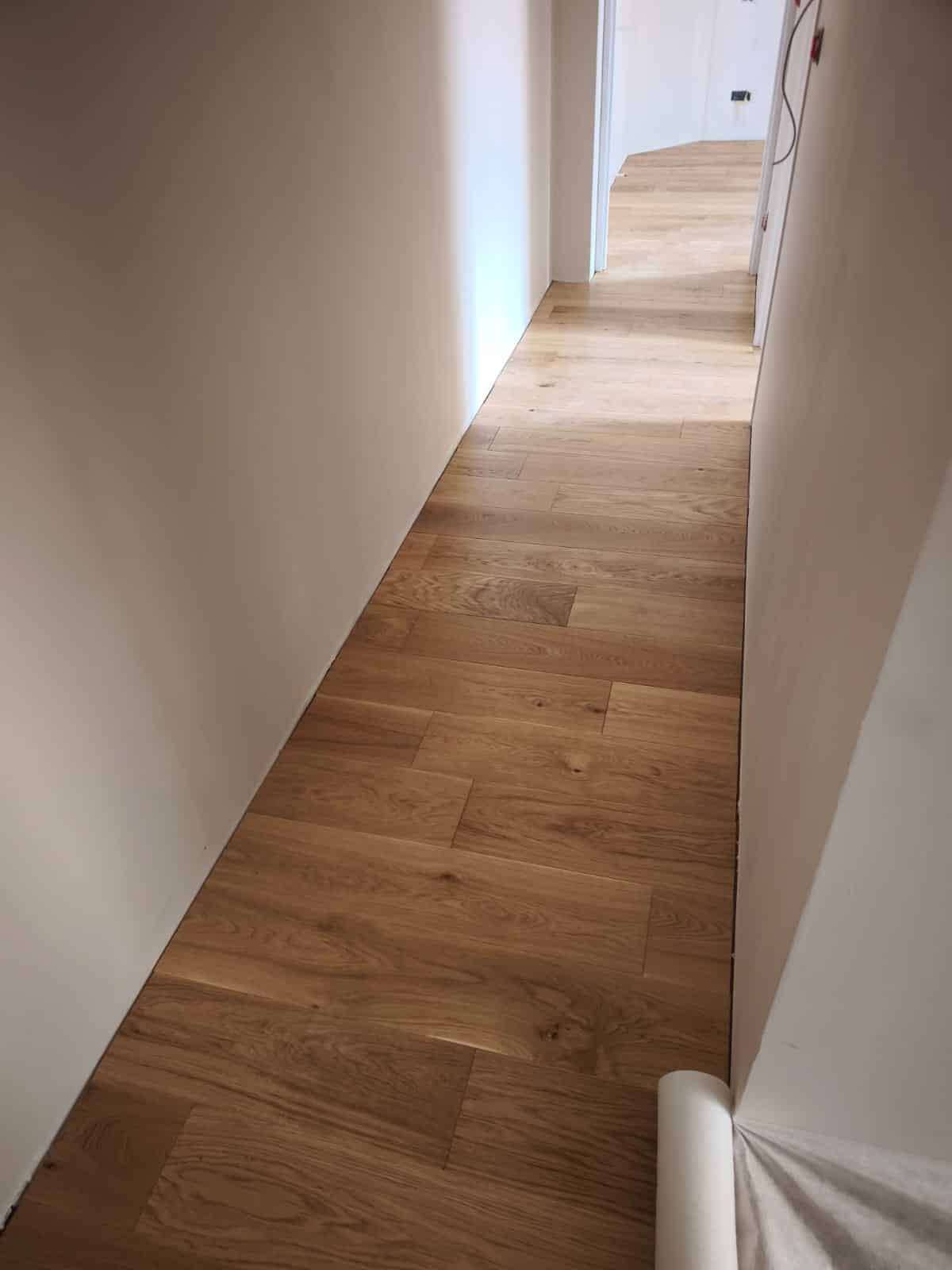 Parquet chêne clair dans un couloir moderne aux murs blancs, vue en perspective lumineuse.