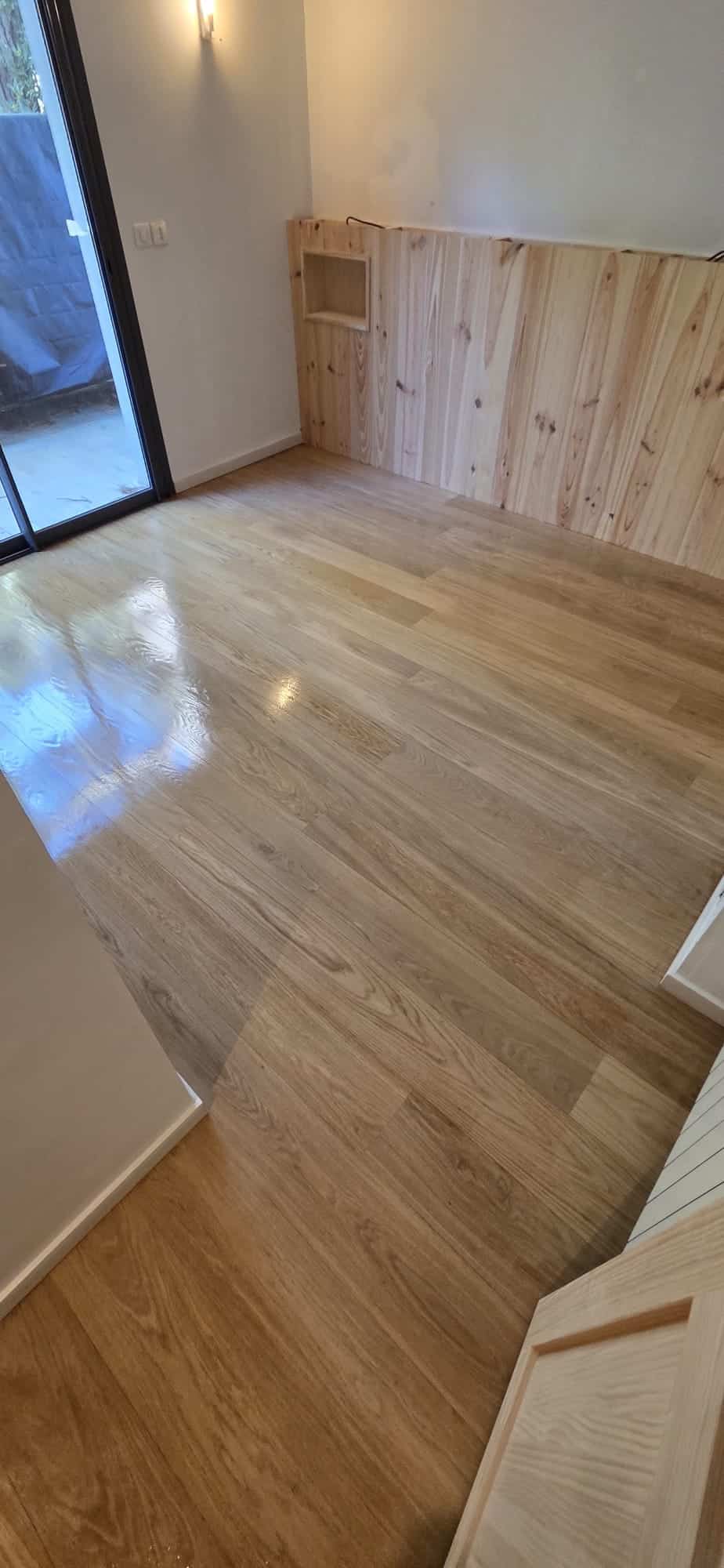 Parquet en chêne clair verni et lambris mural en bois naturel dans une pièce lumineuse.