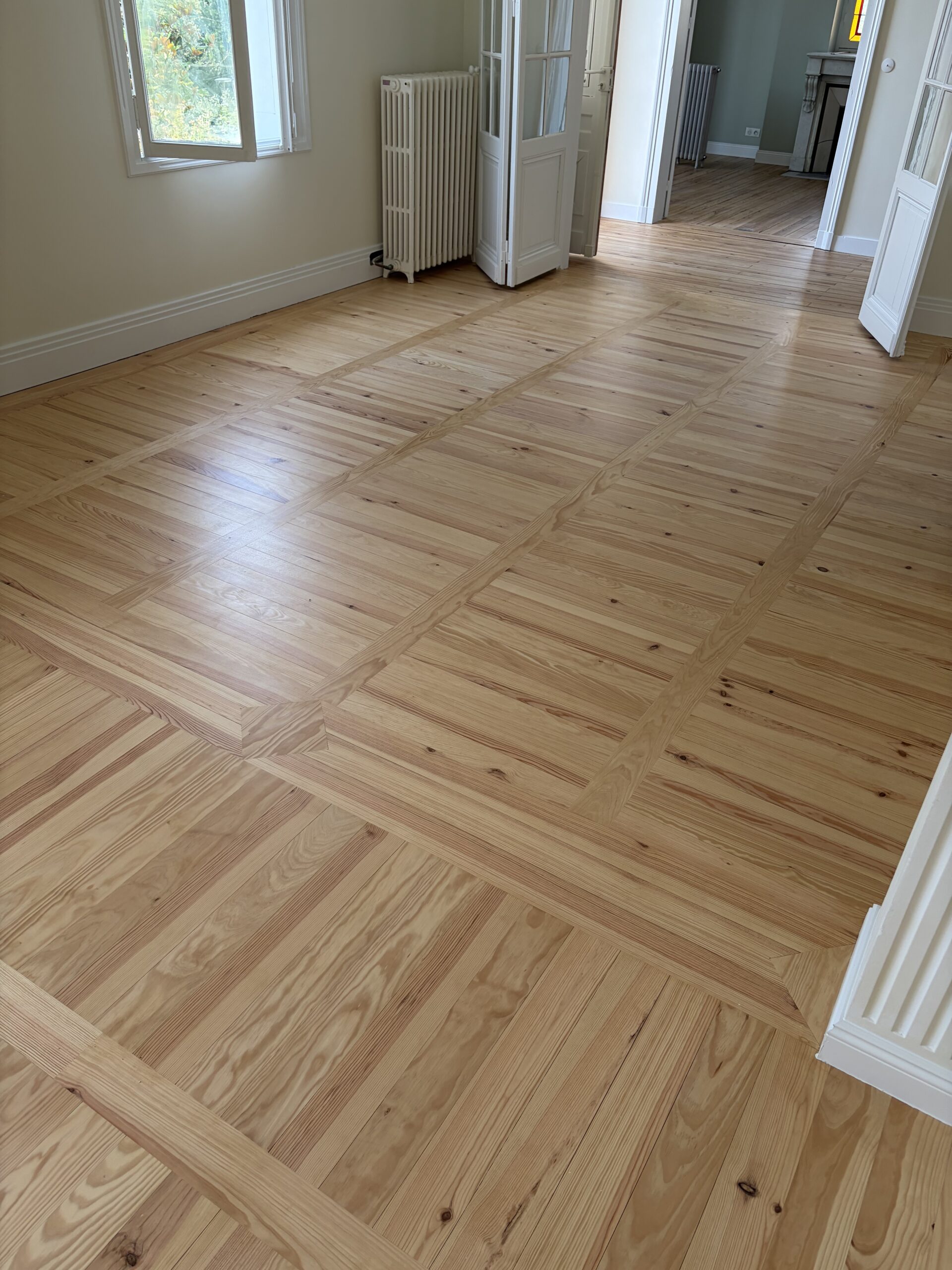 Parquet en pin massif à motifs géométriques dans un intérieur lumineux avec portes blanches.