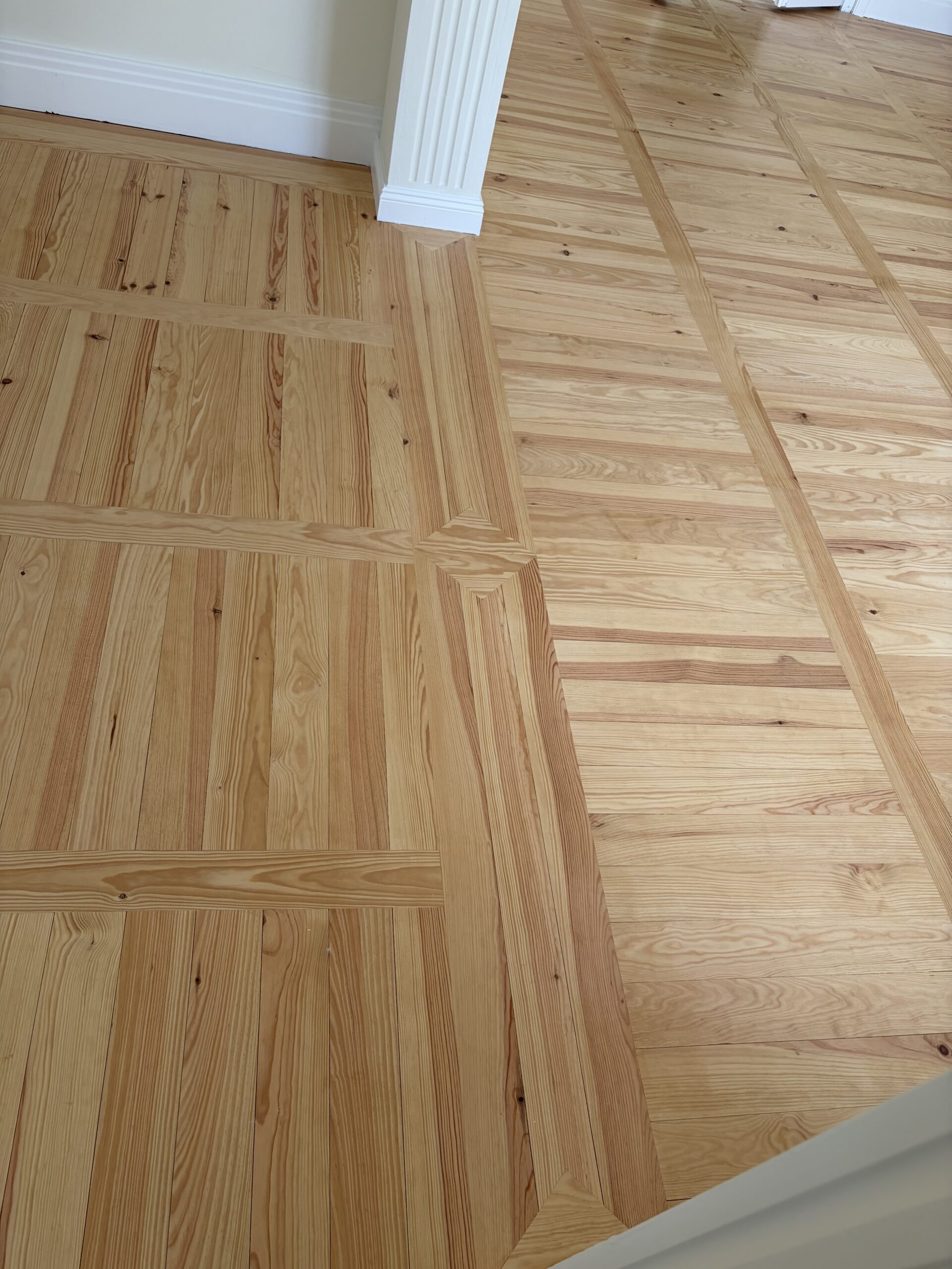 Plancher en pin aux motifs géométriques complexes près d'une colonne blanche cannelée.