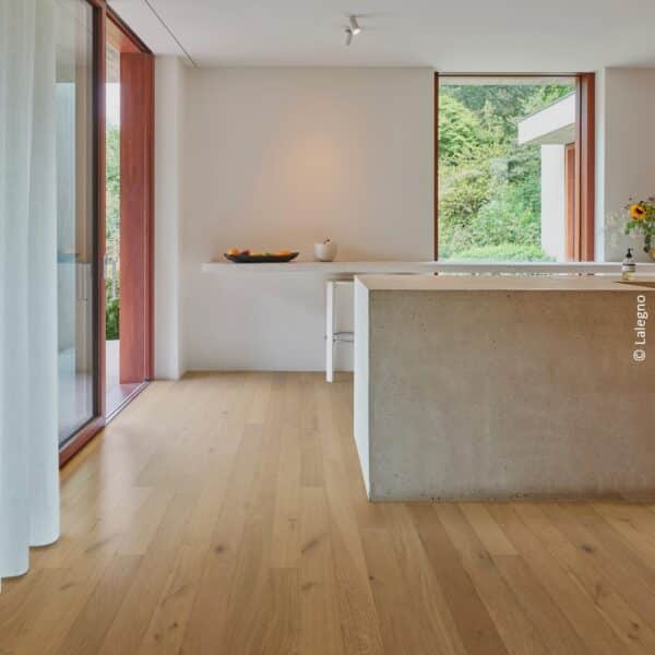 Parquet en chêne clair Lalegno dans une cuisine minimaliste avec îlot central en béton et grandes baies vitrées.