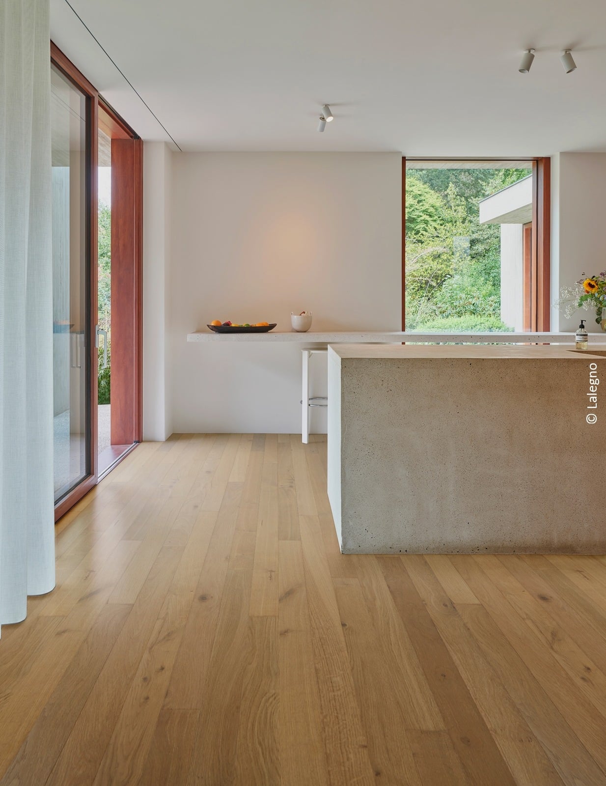 Parquet en chêne clair Lalegno dans une cuisine minimaliste avec îlot central en béton et grandes baies vitrées.