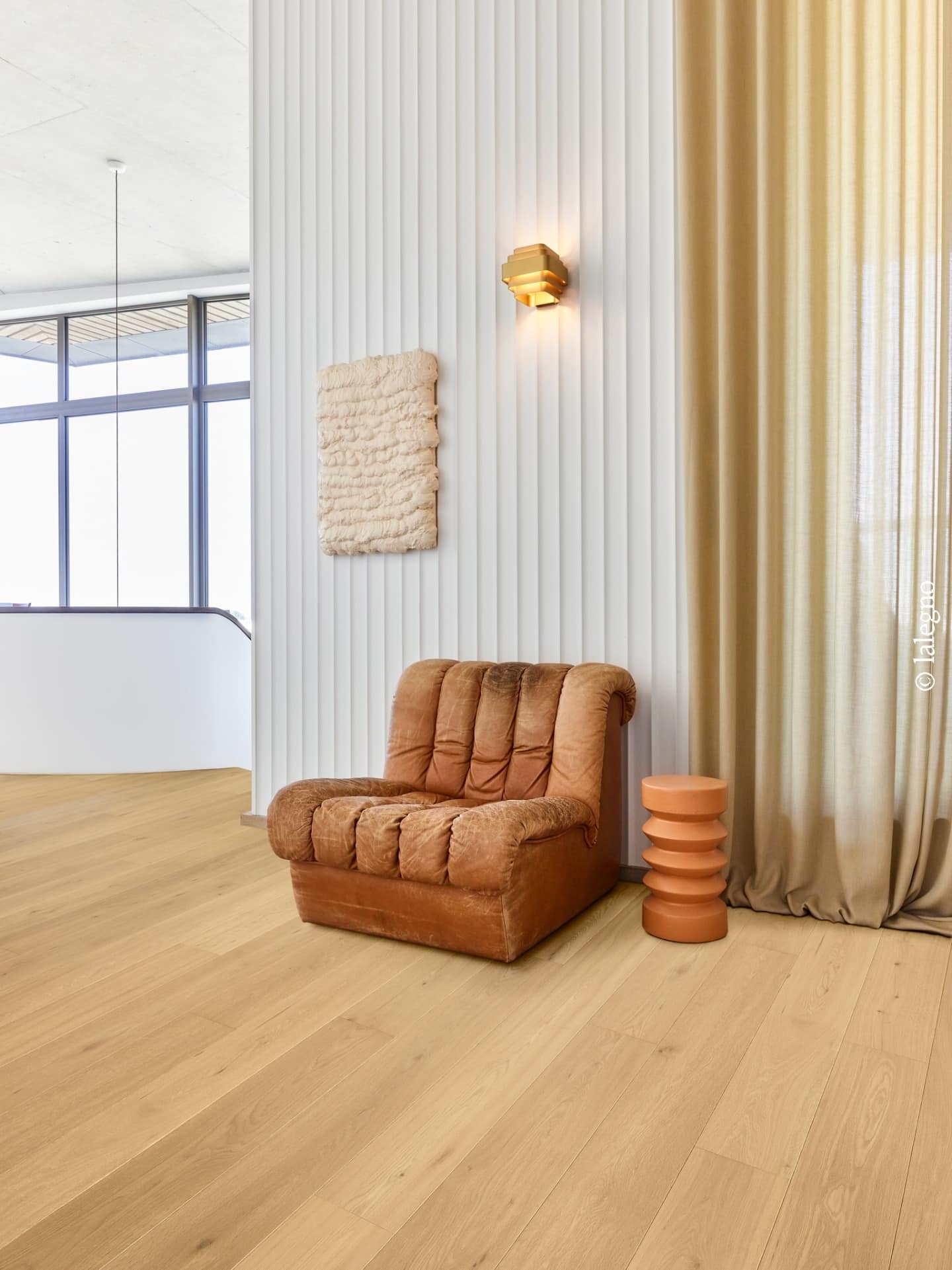 Salon design avec fauteuil cuir marron, parquet en chêne clair Lalegno et décoration murale texturée.
